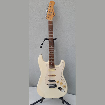 Bílá elektrická kytara typu Stratocaster s hnědým hmatníkem a krčkem z přírodního dřeva. Na hlavě je svisle umístěné logo "LAVA MUSIC". Kytara má tři…