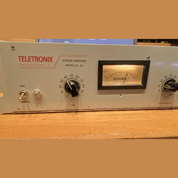 Šedý rackový procesor s nápisy TELETRONIX ENGINEERING CO, LEVELING AMPLIFIER MODEL LA-2A. Zařízení má v pravé části analogový VU metr s nápisem TELET…