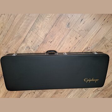 Černý tvrdý kufýr na hudební nástroj s rukojetí a kovovými zapínacími prvky. V pravém dolním rohu je zlatý nápis Epiphone. Povrch kufýru vykazuje dro…