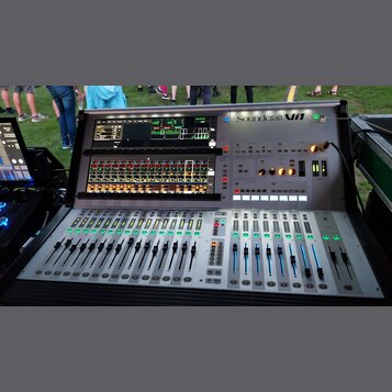 Stříbrný digitální mixážní pult s dvěma vestavěnými displeji. V pravém horním rohu je nápis Soundcraft Vi1. Zařízení obsahuje řadu posuvníků, tlačíte…