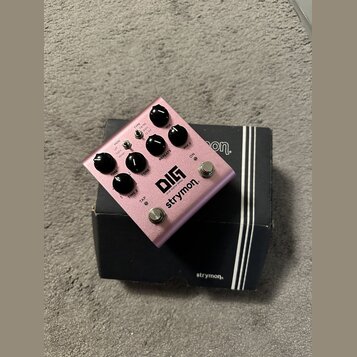 Růžový efekt pedál s nápisy DIG, dual digital delay a strymon. Na horní straně jsou čtyři černé ovládací knoflíky s popisky TIME, TONE, MIX a REPEAT,…