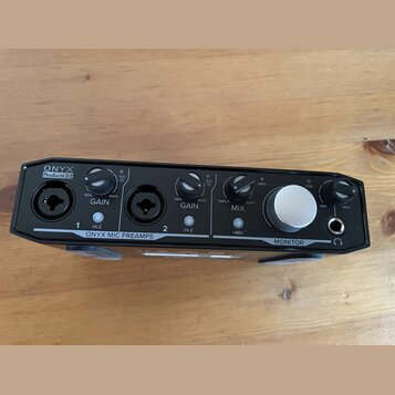 Černý zvukový interface s nápisy ONYX Producer 2-2 a ONYX MIC PREAMPS. Na horní straně jsou dva vstupy, dva ovratidla GAIN s označením MIN a MAX, ovr…