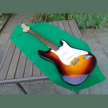 Elektrická kytara s trupem v barevném přechodu od červené přes oranžovou k žluté a bílým pickguardem. Na hlavě hmatníku je nápis Fender Stratocaster.…