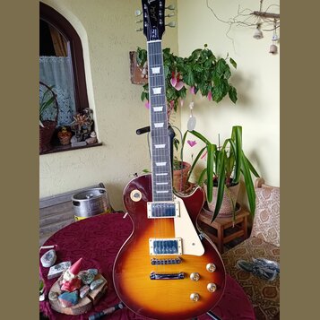 Elektrická kytara typu Les Paul s barevným přechodem od žluté přes oranžovou k červené. Na hlavě hmatníku je nápis "Les Paul Model" a logo značky. Ky…