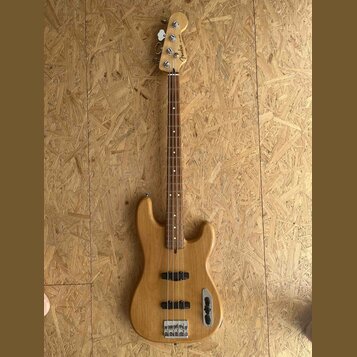 Elektrická basová kytara s přírodním dřevěným povrchem těla a hmatníku. Na hlavě je vidět nápis Fender. Instrument má čtyři struny, dva snímače a jed…