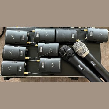 Sada devíti černých bezdrátových vysílačů s nápisem beyerdynamic a logem ve tvaru písmene V. Zařízení jsou umístěna na černém povrchu, z některých ve…