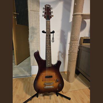 Elektrická kytara s trupem v tmavě hnědém sunburst provedení a hnedým hmatníkem. Na hlavě je bílý nápis „Jolt“. Nástroj má jeden hmatník s kovovými p…