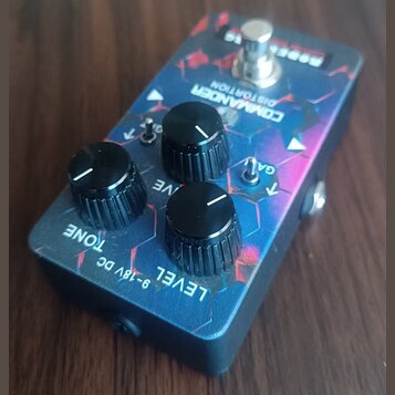 Kytarový efekt s modrým, fialovým a červeným vzorem v podobě šestiúhelníků. Na horní straně je nápis COMMANDER DISTORTION a v pravém horním rohu bílý…