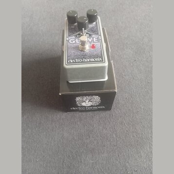 Kytarový efekt v šedém kovovém krytu s nápisem GLOVE a značkou electro-harmonix. Na horní části jsou tři černé ovládací knoflíky s popisky VOL, SHIFT…