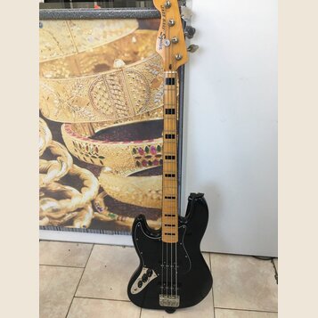 Černá elektrická basová kytara s jasným dřevěným hmatníkem a černými pražcovými značkami. Na hlavě je uveden nápis Squier a Jazz Bass. Tělo je v lesk…