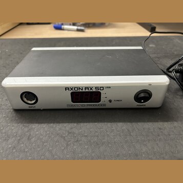 Stříbrno-černý externí zvukový interface s digitálním displejem. Na předním panelu je nápis AXON AX 50 USB a pod displejem označení TERRATEC PRODUCER…