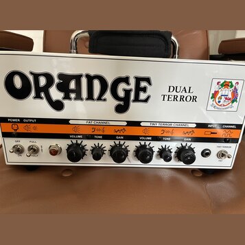 Bílý kytarový zesilovač s oranžovým pruhem uprostřed. Na horní části je černý nápis ORANGE a vedle něj text DUAL TERROR spolu s barevným logem. Předn…