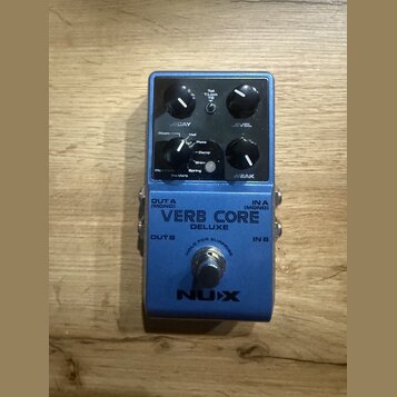 Modrý efekt pedál s nápisy VERB CORE DELUXE a NUX. Na horním panelu jsou dva černé otočné knoflíky s popisky DECAY a LEVEL, přepínač Room/Hall/Plate/…