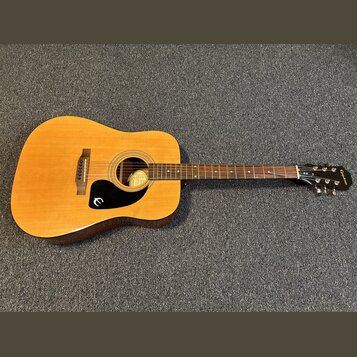 Akustická kytara s přírodním dřevem, tmavě hnědými boky a černým plechtřem. Na hlavě hmatníku je bílý nápis Epiphone. Uvnitř ozvučovacího otvoru je v…