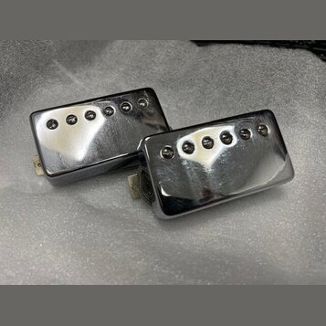 Dvě elektrické kytarové snímače typu humbucker s chromovaným kovovým krytem. Každý snímač má na povrchu šest viditelných polótek. Povrch krytů vykazu…