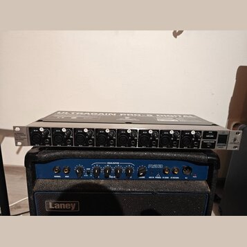 Stříbrné rackové zařízení s nápisem ULTRAGAIN PRO-8 DIGITAL obsahuje osm kanálů s XLR vstupy a ovládacími knoflíky. V pravé části jsou přepínače PHAN…