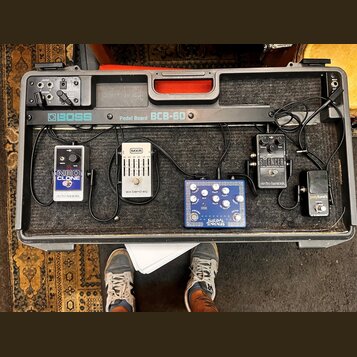 Černý pedalboard značky BOSS, model BCB-60, s několika efektovými pedály. Na desce jsou umístěny pedály s nápisy NEO CLONE electro-harmonix, MXR six…
