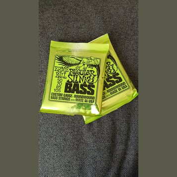 Dvě uzavřená balení basových strun v limegreenovém obalu. Na obalech je černý nápis ERNIE REGULAR BALL SLINKY BASS s rozměry 50, 70, 85, 105 a textem…