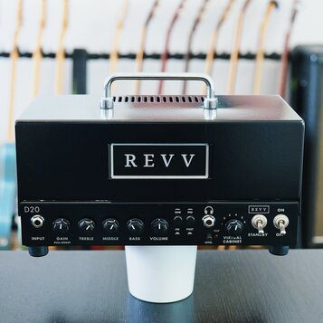 Černý kytarový zesilovač s kovovou rukojetí nahoře. Na předním panelu je bílý obdélníkový štítek s nápisem REVV a vlevo označení D20. Panel obsahuje…