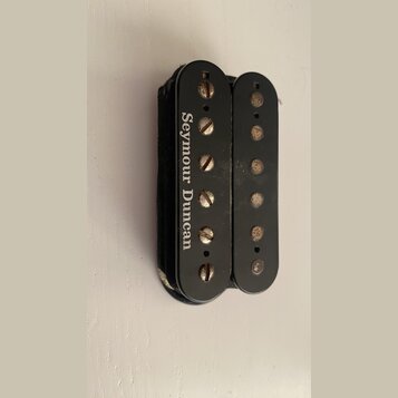 Černý humbucker snímač s dvěma řadami pólů. Na levém krytu je bílý nápis Seymour Duncan. Povrch vykazuje drobné škrábance a opotřebení, zejména u šro…