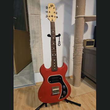 Červená elektrická kytara s dřevěným hmatníkem a světle hnědým hlavním hmatníkem. Na hlavě je nápis "disco plena". Tělo má černý pickguard, dva ováln…