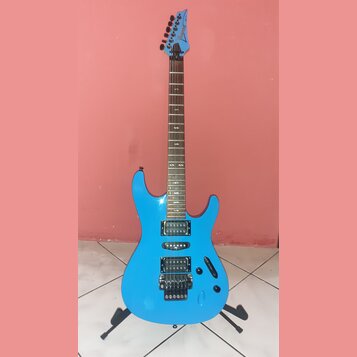 Modrá elektrická kytara s hrazdicem a dvěma humbuckery v pozici kobylníku a krku. Na hlavě hmatníku je bílý nápis Ibanez. Nástroj stojí na černém sto…