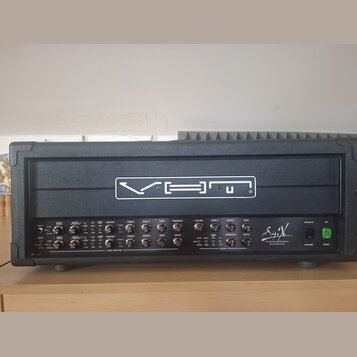 Černý kytarový zesilovač v ochranném kufru. Na horním panelu je bílý nápis VHT a v pravé dolní části logo SigX s doplňkem DYNAMIC SENSING TECHNOLOGY.…