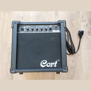Černý kytarový kombo zesilovač značky Cort, model CM10G. Na horním ovládacím panelu jsou nápisy OVERDRIVE, EQUALISATION, POWER, INPUT, GAIN, VOLUME,…