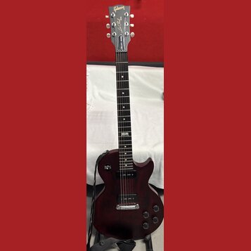 Tmavě červená elektrická kytara typu Les Paul s černým hmatníkem a dvěma humbuckery. Na hlavě je bílý nápis Gibson a pod ním kurzívou Les Paul Model.…