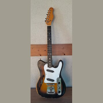 Elektrická kytara s polodupatým korpusem v barevném přechodu od žluté k černé a s bílým pickguardem. Na korpusu je viditelný nápis Jazzmaster a na hl…