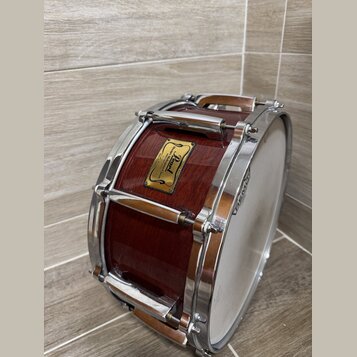 Hnědý dřevěný buben s chromovaným kováním a bílým blátcem. Na korpusu je čtvercový štítek s nápisy „Pearl“, „Master's Idea“ a „Hand-selected Mahogany…