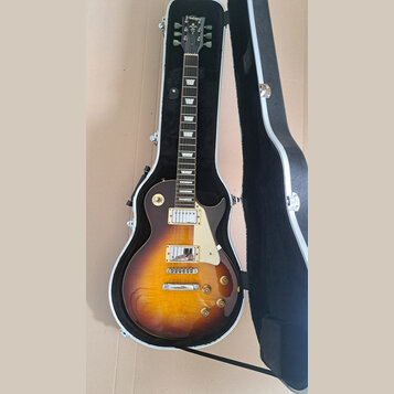Elektrická kytara typu Les Paul s barevným přechodem od žluté k tmavě hnědé v hardcase s černým vnitřkem. Na hlavě je nápis "Vantage". Kytara má dva…