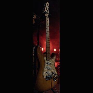 Elektrická kytara s přírodním dřevěným povrchem korpusu a hmatníkem ze světlého dřeva. Kytara má perleťový pickguard a tři snímače typu single-coil.…