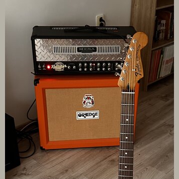 Kytarový zesilovač s nápisem MESA ENGINEERING a modelem DUAL Rectifier NOV WAVE umístěný na oranžovém kytarovém kombu značky ORANGE. Před přístroji s…