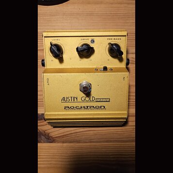 Žlutý kytarový efekt pedál s kovovým tělem. Na přední straně jsou tři černé oválné knofíky s popisky LEVEL, DRIVE a PRE-BASS, přepínač ON a nápisy OU…
