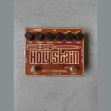 Efektový pedál v hnědo-oranžové barvě s nápisem Holy Stain. Na horní části jsou šest černých otočných ovladačů s popisky MIX, AMOUNT, VOLUME, TONE, C…