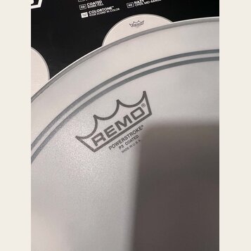 Detailní záběr na bílou, potaženou bicí koženu. Na povrchu je černý nápis REMO s logem koruny a text POWERSTROKE® P3 COATED MADE IN U.S.A. Kožena je…