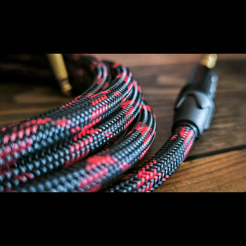 Detailní záběr na svinutý kabel v textilním opletení. Kabel má černou barvu s červenými vzory a je zakončen černým plastovým konektorem. Povrch oplet…