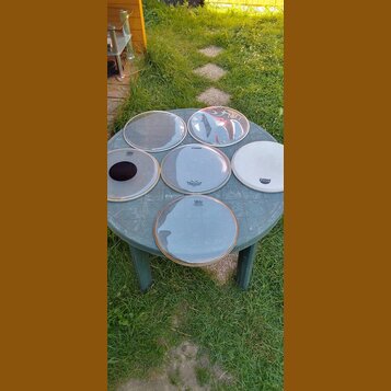 Šest kusů bubnových koží v různých velikostech položených na kulatém plastovém stole. Na kožích jsou vidět nápisy SONOR a REMO. Povrchy jsou průhledn…