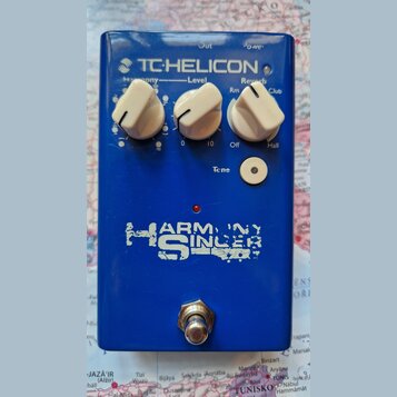 Modrý efekt pedál s nápisem TC-HELICON. Na horní části jsou tři bílé otočné oválkové knoflíky s popisky Harmony, Level a Reverb (s označením Rm, Club…