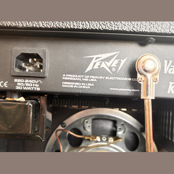 Detail zadní strany kytarového komba s černým povrchem. Je zde vidět napájecí konektor a bílý nápis Peavey s textem A PRODUCT OF PEAVEY ELECTRONICS C…