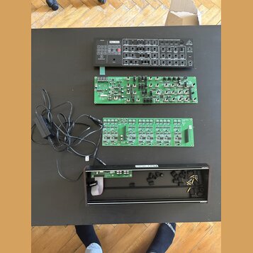 Na černém stole leží rozložený elektronický hudební přístroj. Horní část tvoří ovládací panel s nápisem Pro-1700, řadou tlačítek a zahlreichen potenc…