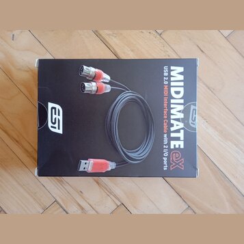 Fotografie znázorňuje černou krabici s produktem. Na obalu je zobrazen USB-MIDI kabel a nápisy MIDIMATE eX, USB 2.0 MIDI Interface Cable with 2 I/O p…