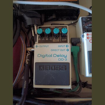 Kytarový efekt pedál Boss Digital Delay DD-3 v bílo-šedém provedení. Na horní části jsou čtyři modré ovládací knoflíky a nápisy CHECK, L 800ms HOLD,…
