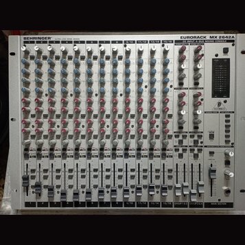 Stříbrný míchací pult s nápisy BEHRINGER® ULTRA-LOW NOISE DESIGN a EURORACK MX 2642A 26 INPUT 4-BUS MIXING CONSOLE. Zařízení obsahuje řady šedých, mo…