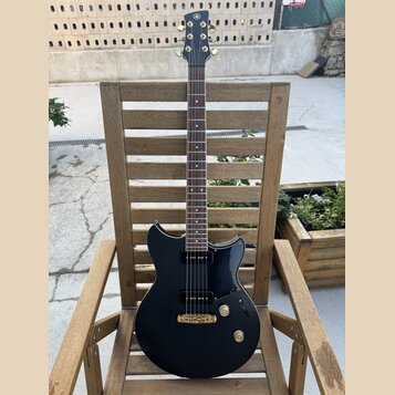 Černá elektrická kytara s tmavým hmatníkem a zlatými prvky. Na hlavě je viditelné logo Yamaha, na korpusu jsou dva humbuckery a tři ovládací knoflíky…