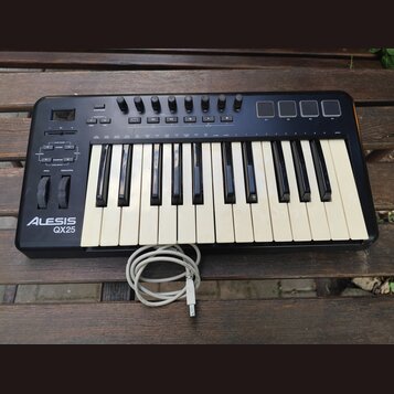 Černý kompaktní MIDI kontrolér s klávesnicí, umístěný na dřevěném stole. Na levé straně je bílý nápis ALESIS QX25 a ovládací prvky v podobě tlačítek,…