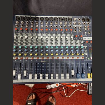 Modrý mixovací pult s kovovým šasi a řadou vertikálních posuvníků. V pravém horním rohu je nápis Soundcraft a dále modelové označení EPM12. Zařízení…