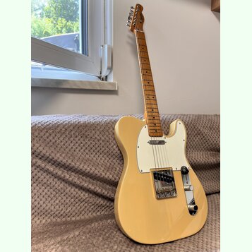 Elektrická kytara typu Telecaster v krémové barvě s bílým pickguardem. Na hlavě hmatníku je viditelné logo Fender. Nástroj je vybaven stříbrným moste…