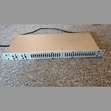 Bíle provedený rackový grafický ekvalizér s řadou posuvníků. Na levé straně je nápis DUAL 15 BAND GRAPHIC EQUALIZER MODEL Q-15 a logo Q. Vpravo je uv…